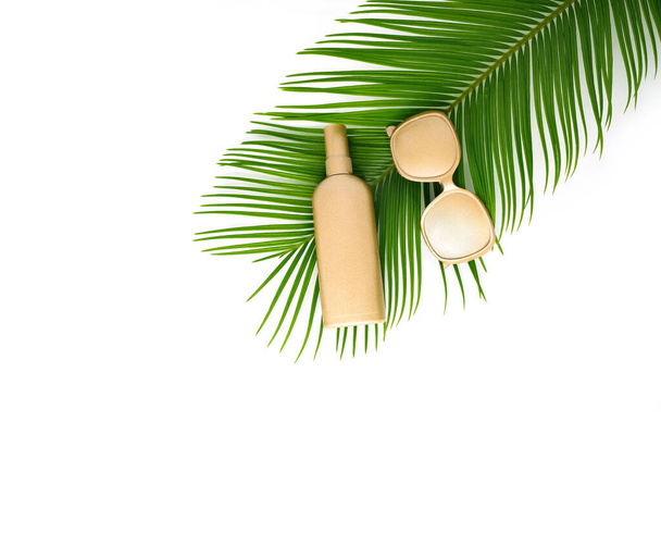 Golden cream bottle, sunglasses and tropical leaf on the white background. - Foto, Imagen
