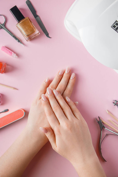 Спа-процедури по догляду за нігтями в салоні краси. Жіночі руки та інструменти для манікюру на рожевому тлі. концепція догляду за тілом
. - Фото, зображення