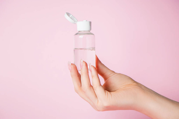 Manos femeninas con una botella de crema sobre un fondo rosa. Spa y concepto de cuidado corporal. Imagen para publicidad. - Foto, Imagen