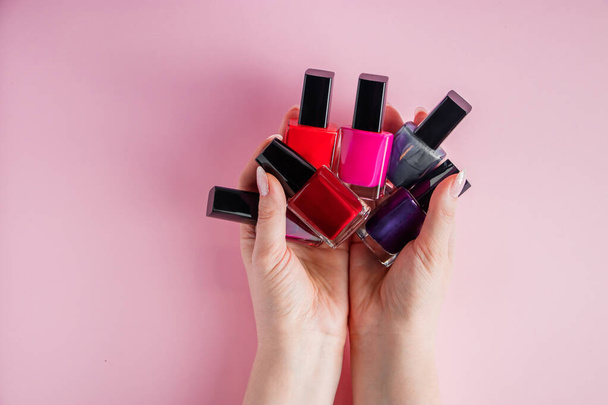 Vrouwelijke handen met heldere nagellakken. Een groep gekleurde nagellak op een roze achtergrond. - Foto, afbeelding