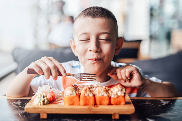 Мальчику нравится есть суши-роллы в кафе на открытом воздухе - Фото, изображение