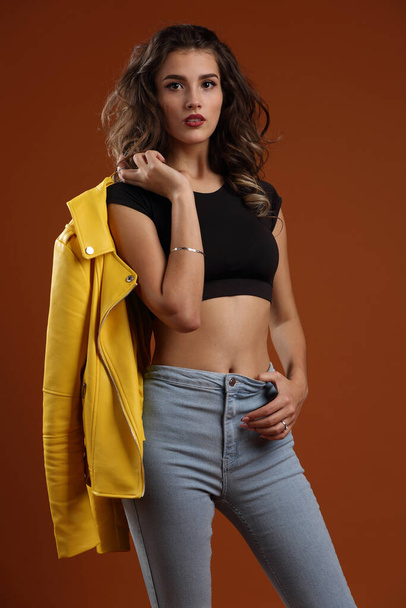 Beautiful girl in a black top, blue jeans and a jacket on a brown background - Zdjęcie, obraz