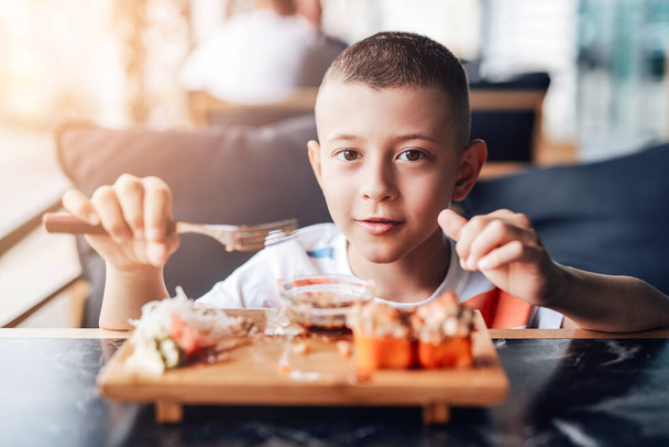 Мальчику нравится есть суши-роллы в кафе на открытом воздухе - Фото, изображение