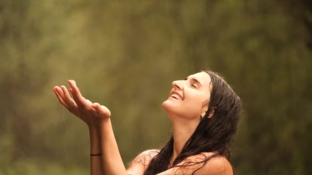 Mouvement lent d'une jeune femme heureuse attrayante avec les yeux fermés attrape des gouttes de pluie avec ses paumes et profite du moment. - Séquence, vidéo