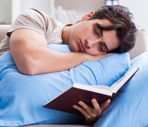 Νεαρός φοιτητής προετοιμάζεται για τις εξετάσεις κολέγιο στο κρεβάτι με το βιβλίο - Φωτογραφία, εικόνα