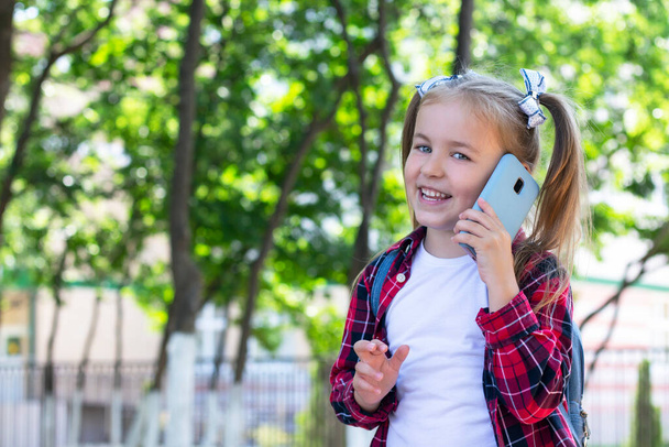 happy schoolgirl with a backpack talking on the phone on the street. in a white T-shirt and a plaid shirt - Foto, immagini