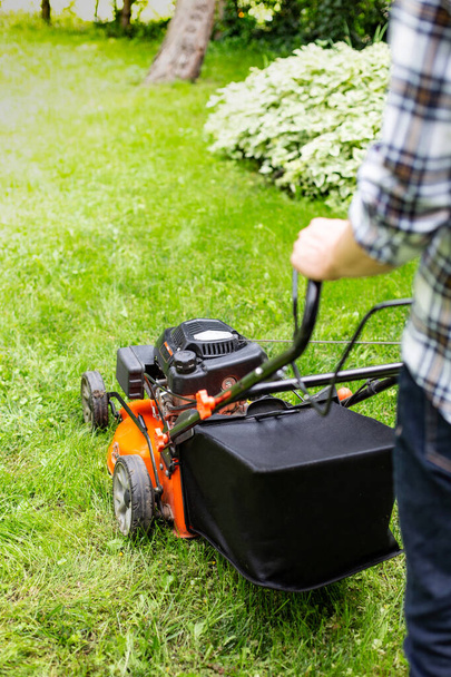 Gardening. Greenworks. Man mowing grass using a petrol lawnmower with a high-capacity grass box. Mowing a lush, leafy green lawn by motor mower, gasoline lawnmower in a garden on a sunny day - Foto, immagini