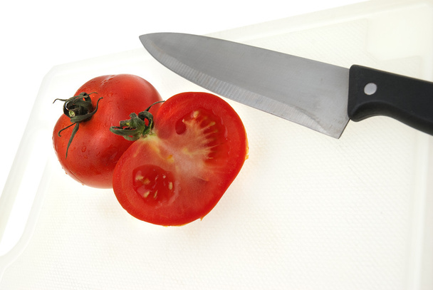 Corte de placa de plástico branco com uma faca e tomate
 - Foto, Imagem