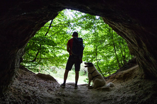 man and dog silhouette at the entrance of a cave - Photo, Image