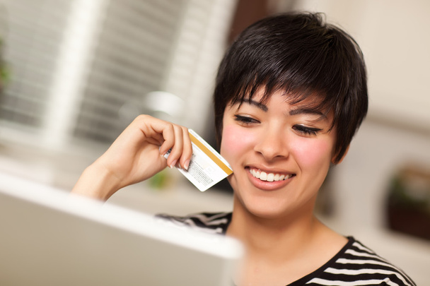 Улыбающаяся многонациональная женщина держит кредитную карту с помощью ноутбука
 - Фото, изображение