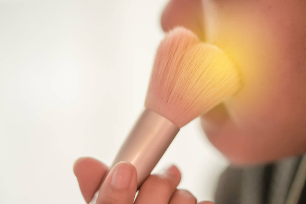 Pretty girl is applying blush on cheek by brush. Beauty Makeup. - Zdjęcie, obraz