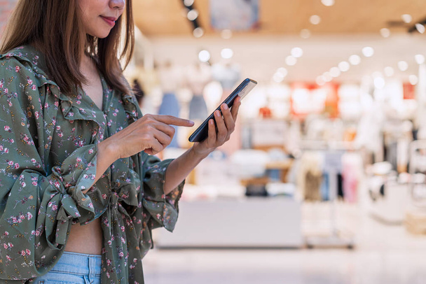 Joven mujer asiática con bolsas de compras usando teléfono inteligente y compras en el centro comercial, concepto de estilo de vida de la mujer - Foto, imagen