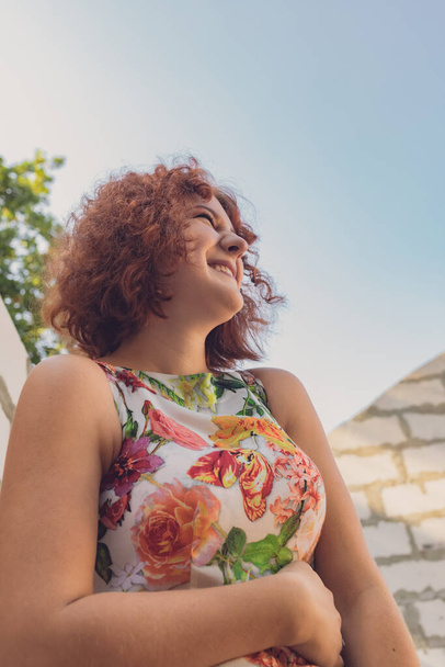 red-haired curly-haired girl in a summer dress posing in the village  - 写真・画像