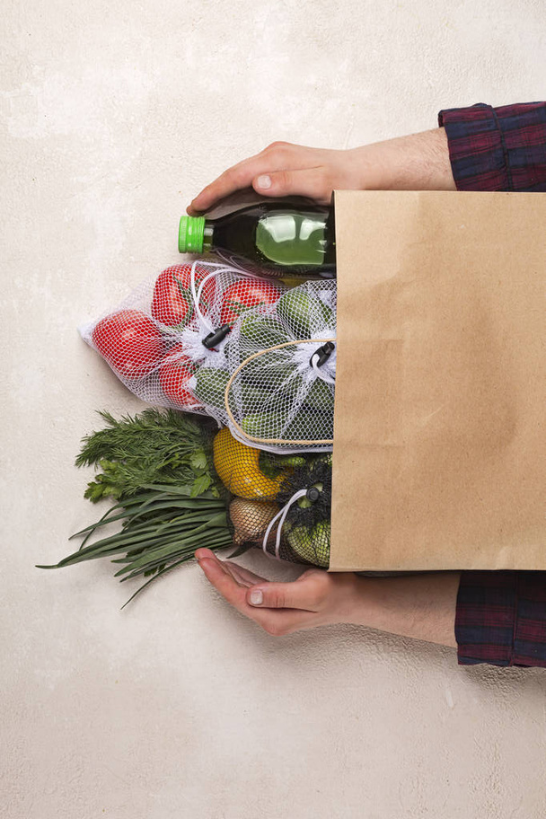Man holds products in a paper bag. Vegetables in the range of shopping in the terrestrial and online store. - Fotografie, Obrázek