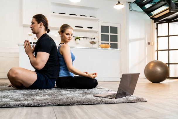 White caucasian fit sporty couple doing yoga Sukhasana sit pose in living room at home watching online tutorials from trainer on laptop. Working out, fitness sport and healthy lifestyle concept. - Fotoğraf, Görsel
