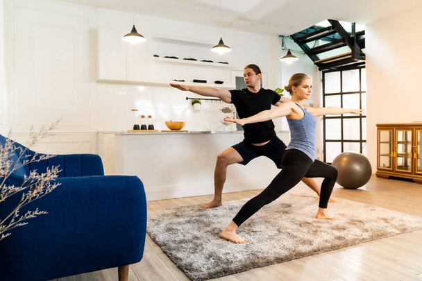 White caucasian fit sporty couple doing yoga warrior pose in living room at home. Working out, fitness sport and healthy lifestyle concept. - Fotoğraf, Görsel