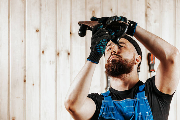 Muž stavební dělník v černé špinavé konstrukci celkově uzavírá šroub s černým moderním šroubovákem v dřevěném bloku v dílně - Fotografie, Obrázek