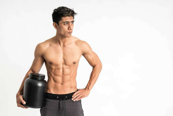 asian young man with muscular body carry a black bottle with one hand stand facing forward and look to side - Fotografie, Obrázek