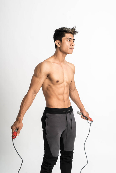 Молодой человек с мускулистым телом держит скакалку с двумя руками стоять лицом вперед и смотреть в сторону - Фото, изображение