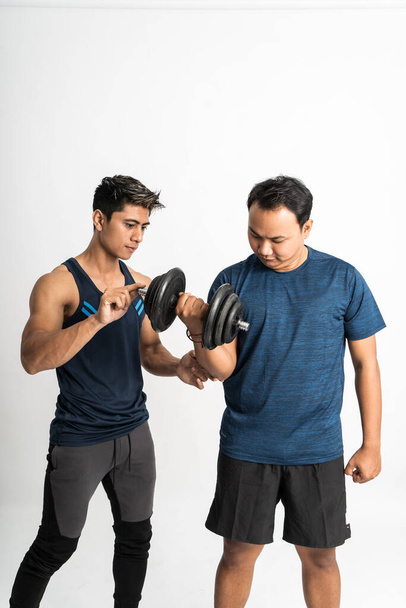 trainer accompanies a man lifting dumbbell for biceps exercises with holding hand to make the right moves - Foto, afbeelding
