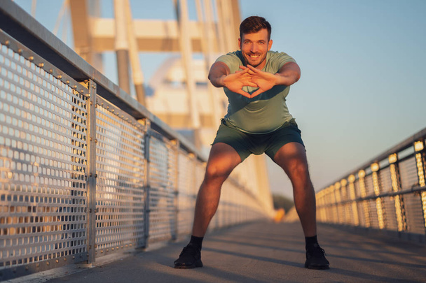 Young man is exercising outdoor on bridge in the city. - Photo, Image