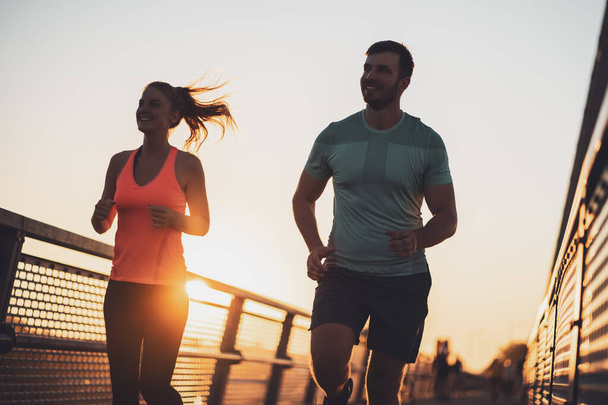 jong paar is joggen in de stad in zonsondergang. - Foto, afbeelding