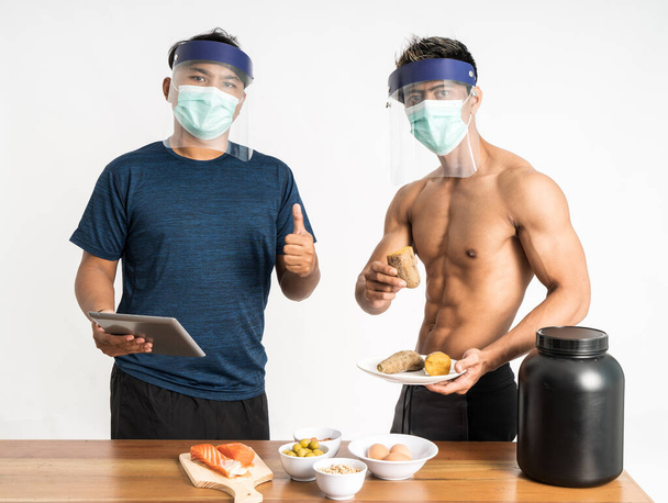 dva asijské zdraví a sportovní blogger nosí masku a obličejový štít s palci nahoru ukazující zdravé jídlo menu při držení tablet - Fotografie, Obrázek