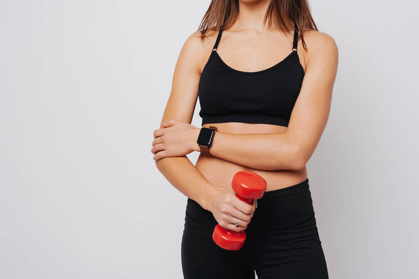 Woman is holding a red dumbbel wearing a fitness watch - Zdjęcie, obraz