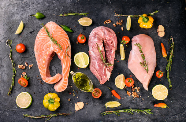 Fresh and healthy food of meat and fish. Chicken fillet, pork, trout steak, spices, sprigs of razmarin, lime, olive oil, vegetables. View from above - Photo, Image
