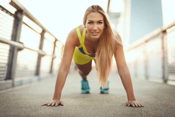 Νεαρή γυναίκα γυμναστικής κάνει push-up ή σανίδα άσκηση στο river bridge κατά τη διάρκεια της πρωινής προπόνηση. - Φωτογραφία, εικόνα