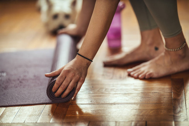 Gros plan d'une main de femme roule tapis d'exercice et se prépare à faire du yoga.  - Photo, image