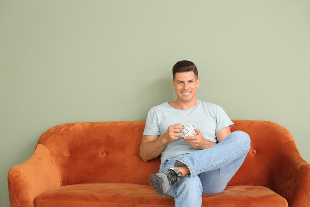 Young man with tea relaxing on sofa near color wall - Fotografie, Obrázek