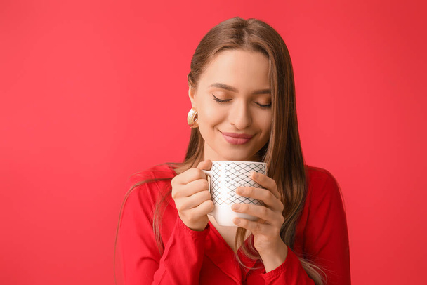 Belle jeune femme avec tasse de thé sur fond de couleur - Photo, image
