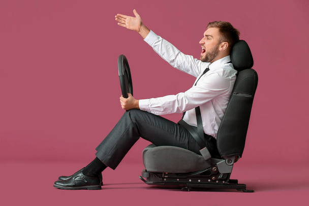 Displeased young businessman with steering wheel sitting on car seat against color background - Photo, Image