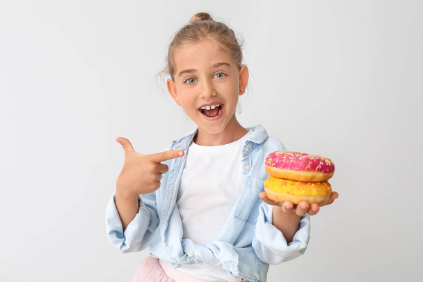 Grappig klein meisje met donuts op lichte achtergrond - Foto, afbeelding