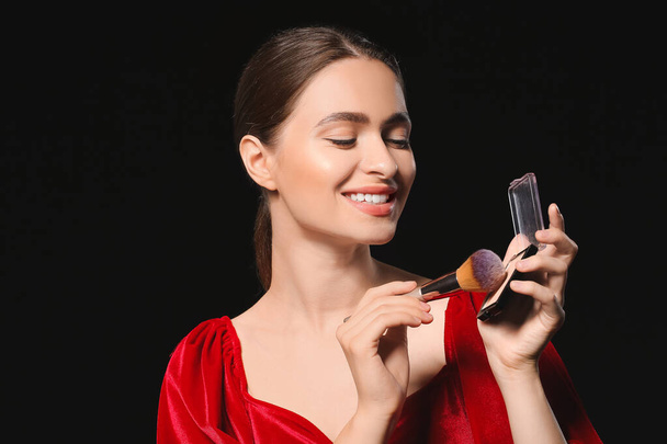 Young woman doing makeup on dark background - Foto, afbeelding