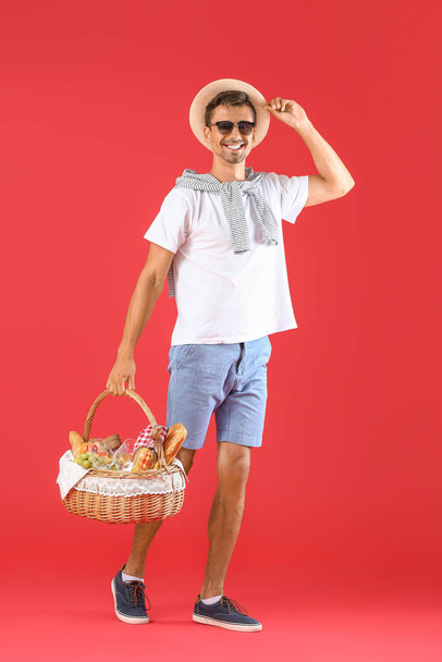 Jongeman met eten voor picknick in mand op kleur achtergrond - Foto, afbeelding
