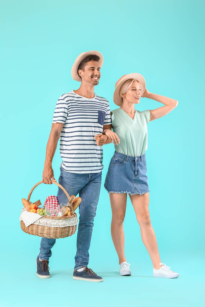 jong paar met voedsel voor picknick in mand op kleur achtergrond - Foto, afbeelding