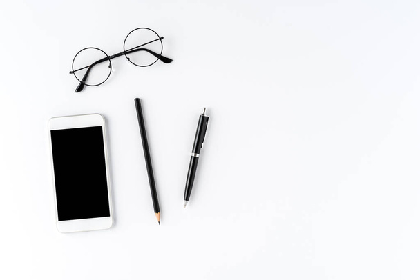 Smartphone, eyeglasses and pens on white desktop. Business background - Фото, изображение