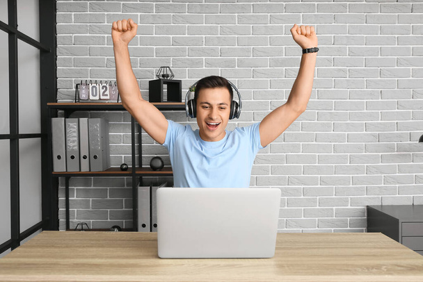 Happy man with headphones and laptop working in office - Photo, Image