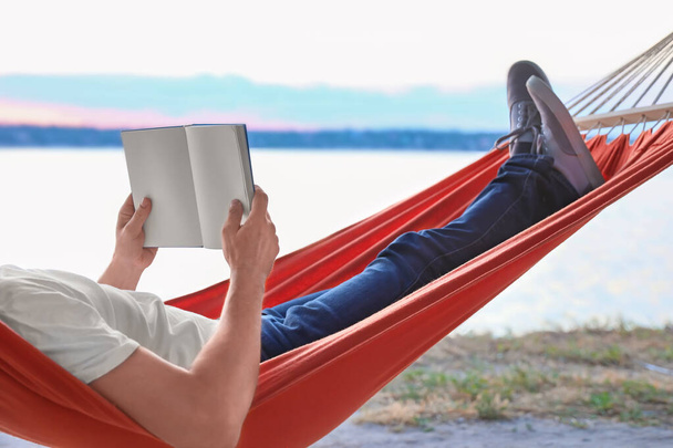 Jongeman lezen boek tijdens het ontspannen in hangmat buiten - Foto, afbeelding