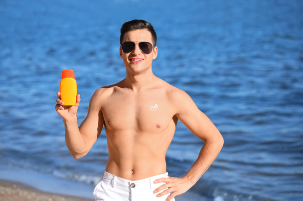 Schöner junger Mann mit Sonnencreme am Strand - Foto, Bild