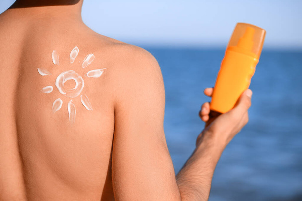 Schöner junger Mann trägt Sonnencreme am Strand auf - Foto, Bild