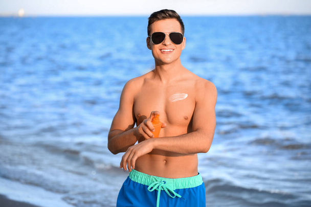Knappe jongeman die zonnebrandcrème aanbrengt op het strand - Foto, afbeelding