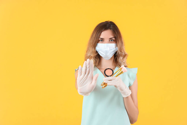 Женщина визажистка с медицинской маской показывает стоп-жест на цветном фоне. Эпидемия коронавируса - Фото, изображение
