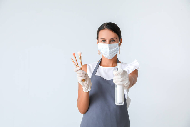 Female makeup artist wearing medical mask on light background. Coronavirus epidemic - Zdjęcie, obraz