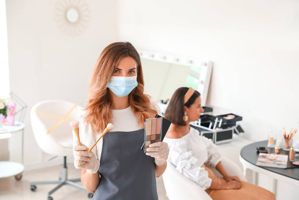 Vrouwelijke make-up kunstenaar met medisch masker in salon tijdens coronavirus epidemie - Foto, afbeelding