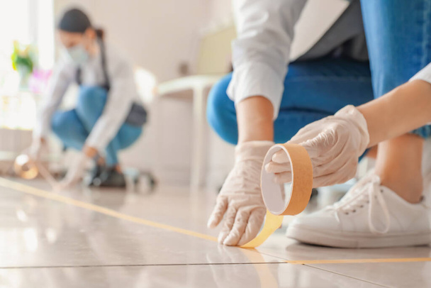 Samičí maskérka nanáší pásku na podlahu v salonu během epidemie koronaviru - Fotografie, Obrázek