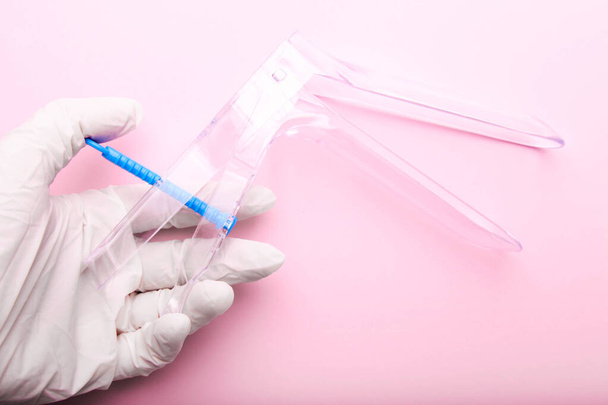 Disposable gynecological speculum in a female hand on a pink background. - Photo, Image