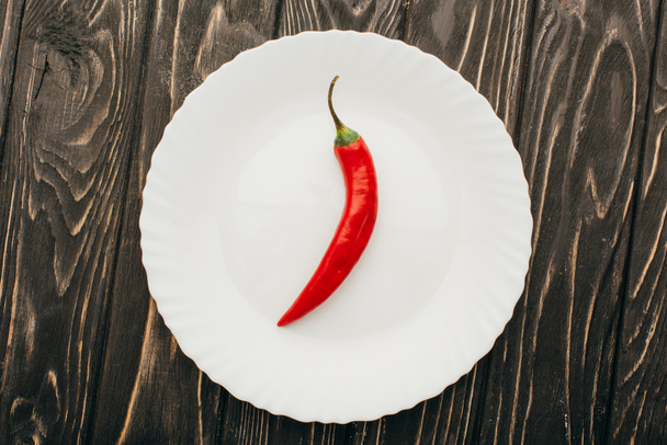 ylhäältä näkymä punainen chili pippuri valkoinen levy puupinnalla - Valokuva, kuva